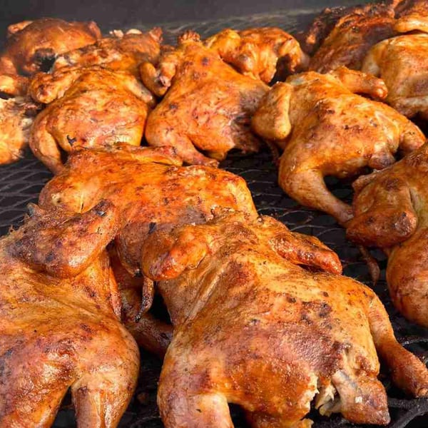 Numerous whole roasted chickens with crispy, golden-brown skin cooking on a grill grate.