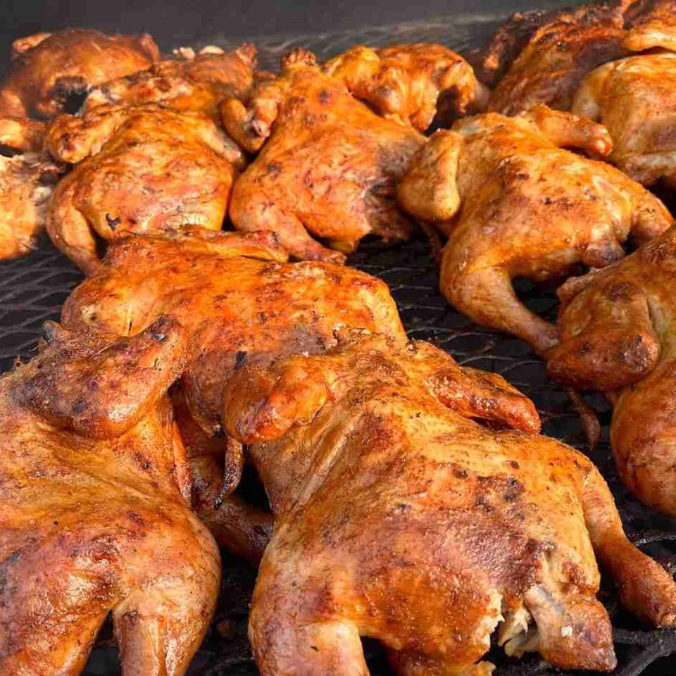 Numerous whole roasted chickens with crispy, golden-brown skin cooking on a grill grate.