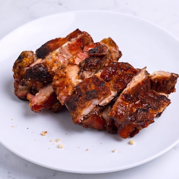 Sliced, charred grilled meat arranged on a white plate, with crispy browned edges and visible juices.