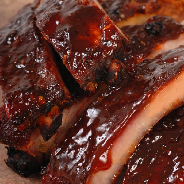 Close-up of juicy, saucy BBQ ribs with glistening dark red sauce covering the meat.