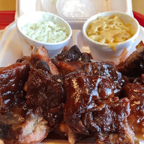 Barbecue ribs with a side of coleslaw and macaroni and cheese in a takeout container.